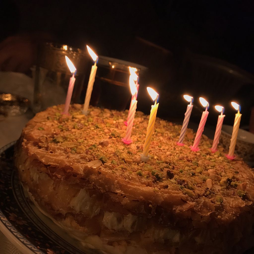 Bougies allumées plantées dans une pastilla au lait aux amandes et pistaches, salle sombre en arrière-plan