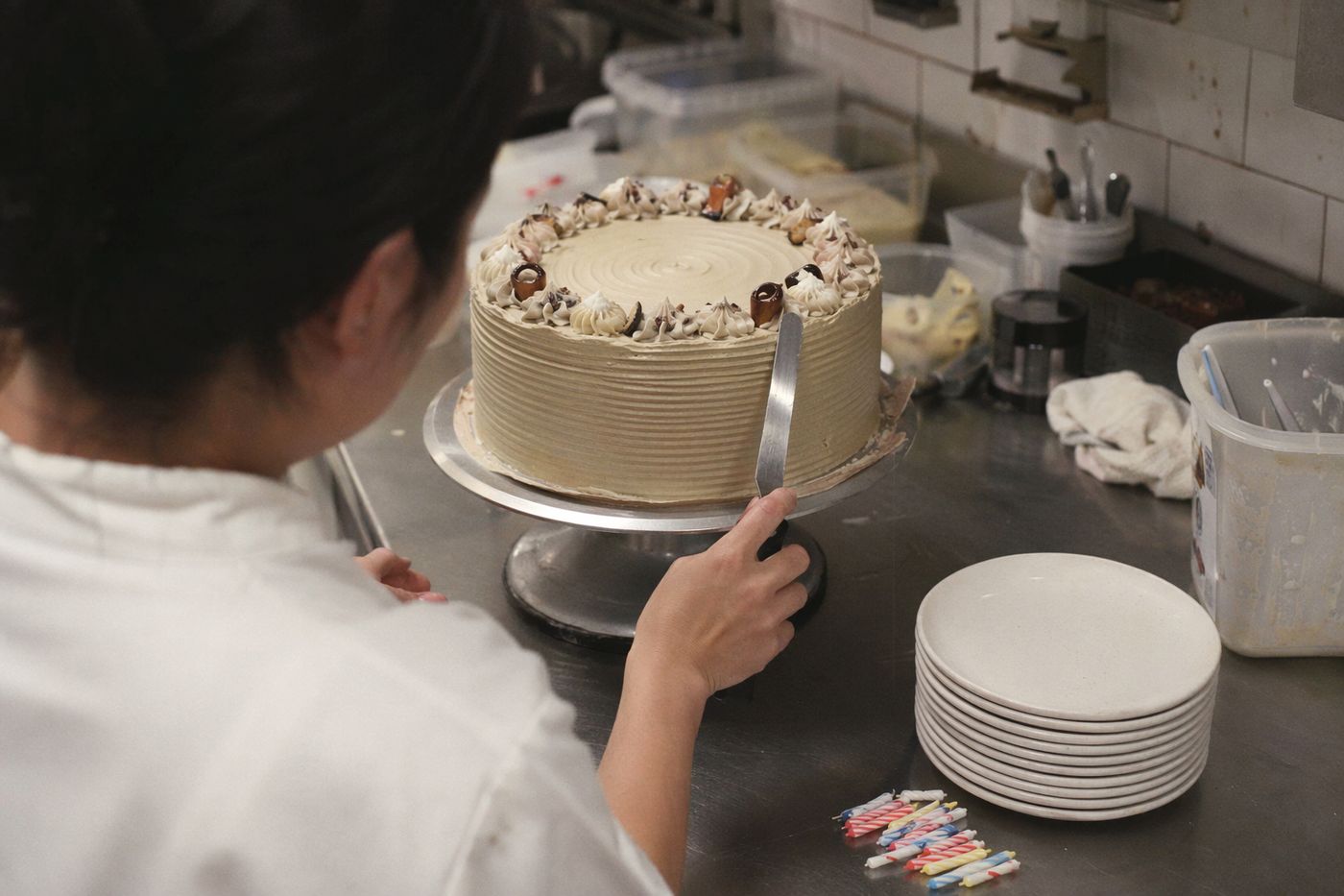 Mains d'un pâtissier lissant un gâteau de fête en cuisine, assiettes et bougies prêtes à côté