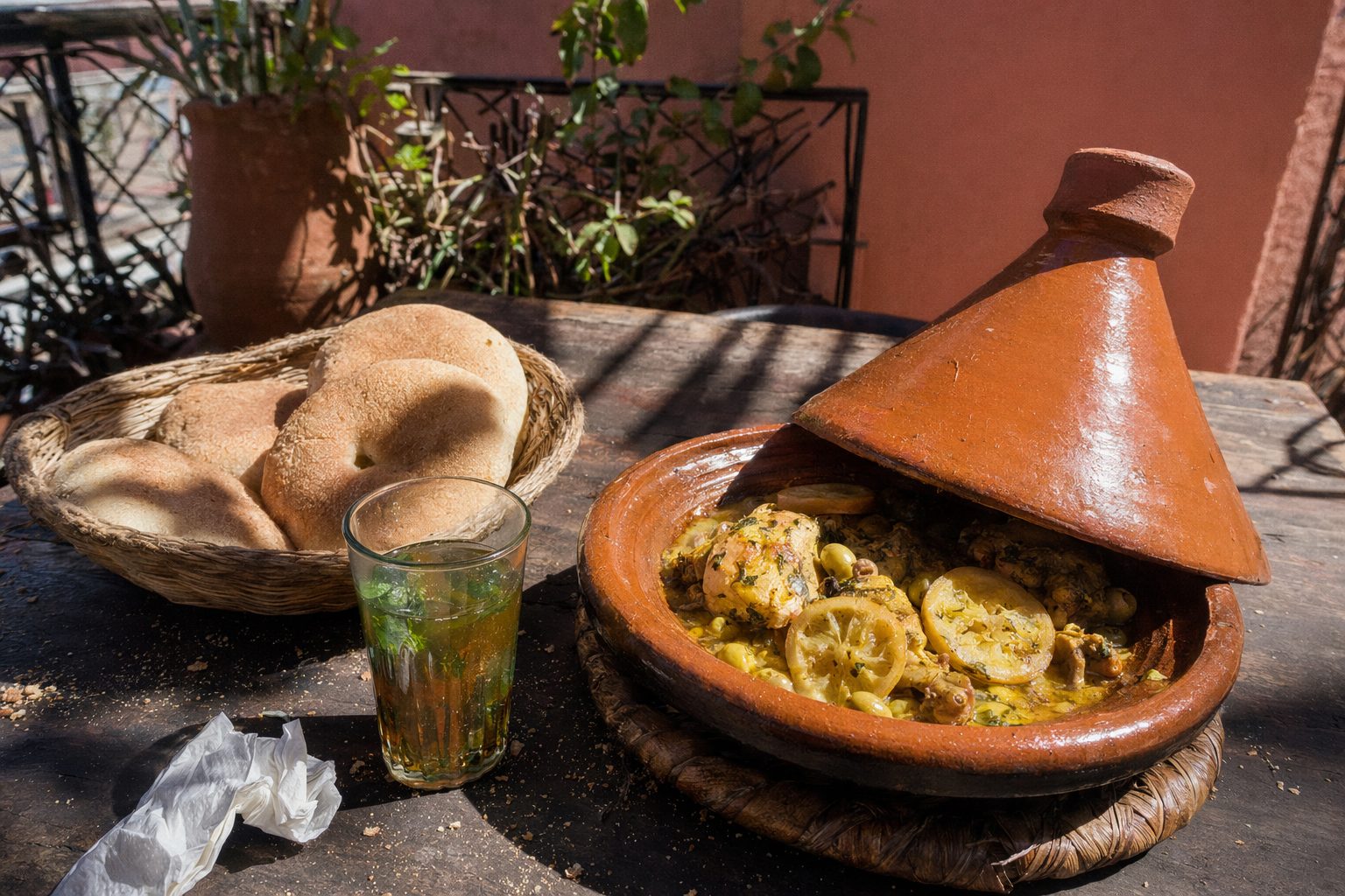 Tajine de poulet au citron, pain et thé à la menthe sur une table simple en plein soleil de midi.