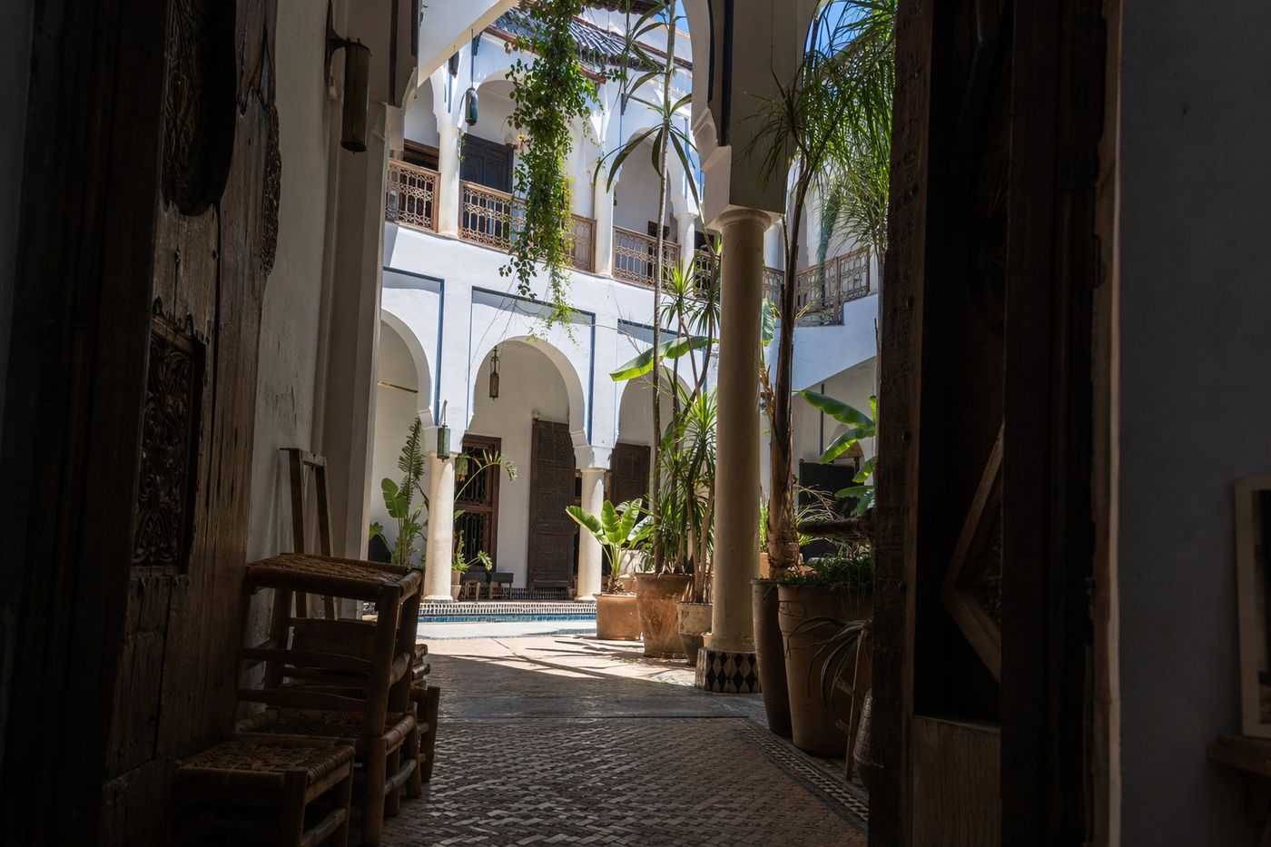 Cour de riad vue d'une porte, lumière de midi descendant le long des galeries carrelées.