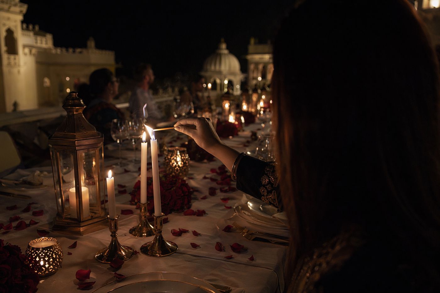 Main allumant des bougies sur une table de palais parsemée de pétales de rose, le soir.