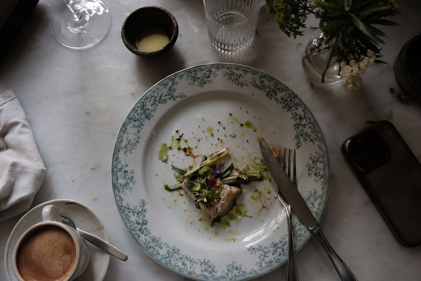 Vue du dessus d'une table stylisée : assiette décorative à peine entamée et café refroidi.