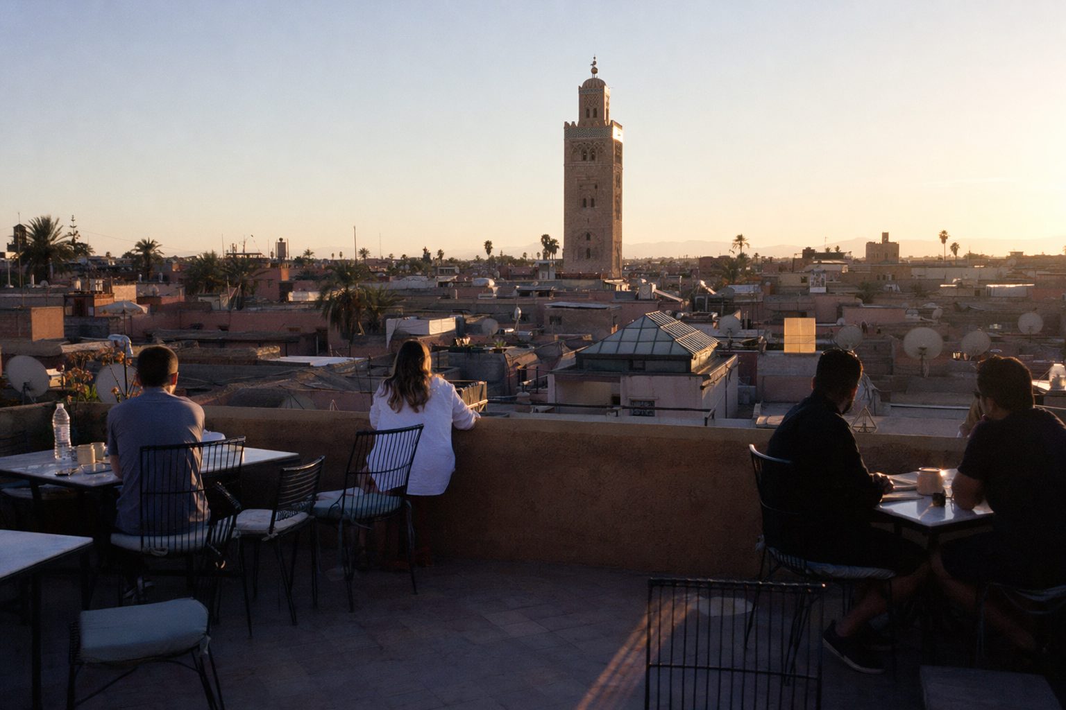 Terrasse de toit face à un minaret au soleil couchant, silhouettes de dos au parapet.