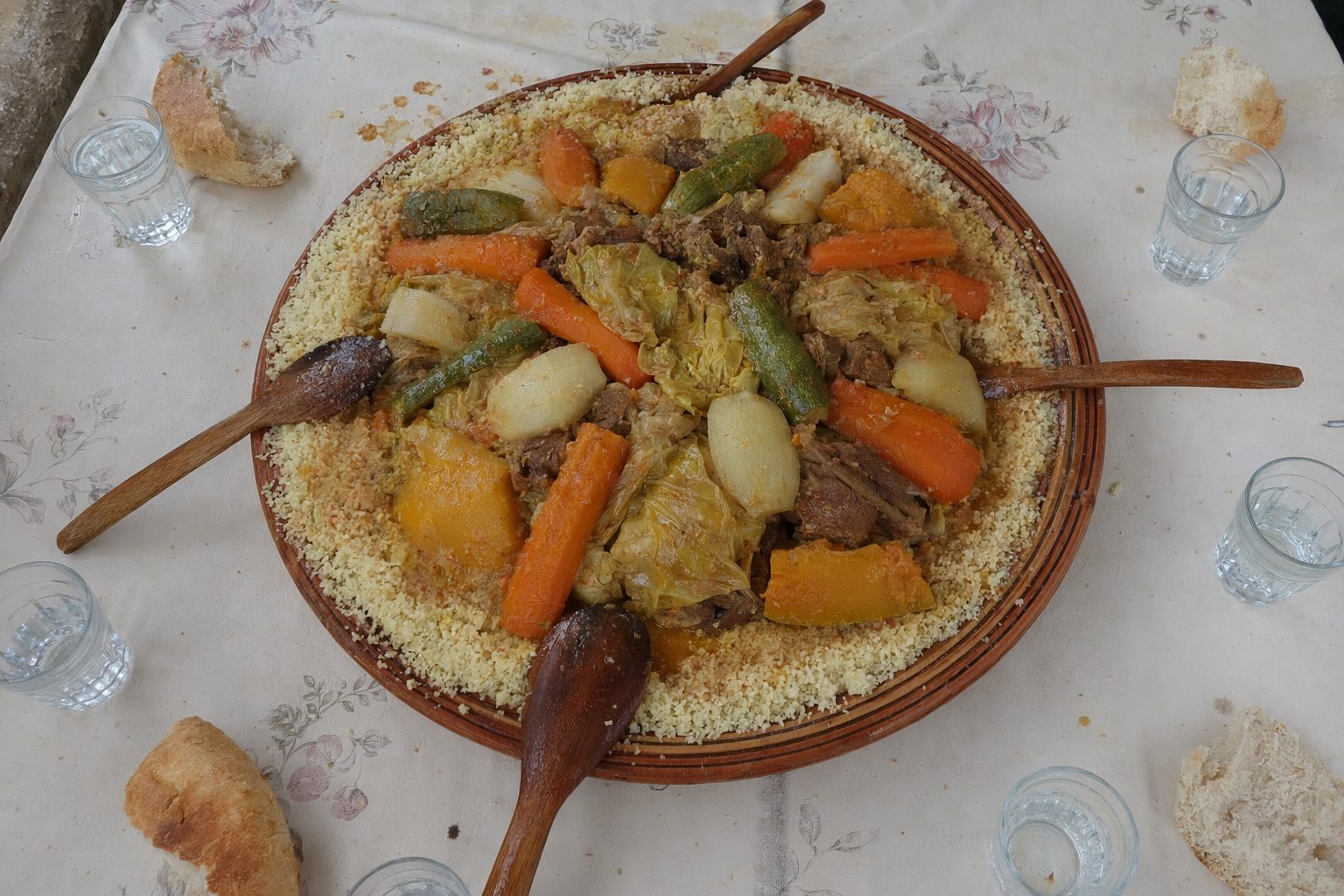 Grand plat commun de couscous aux sept légumes vu du dessus, cuillers en bois posées tout autour.