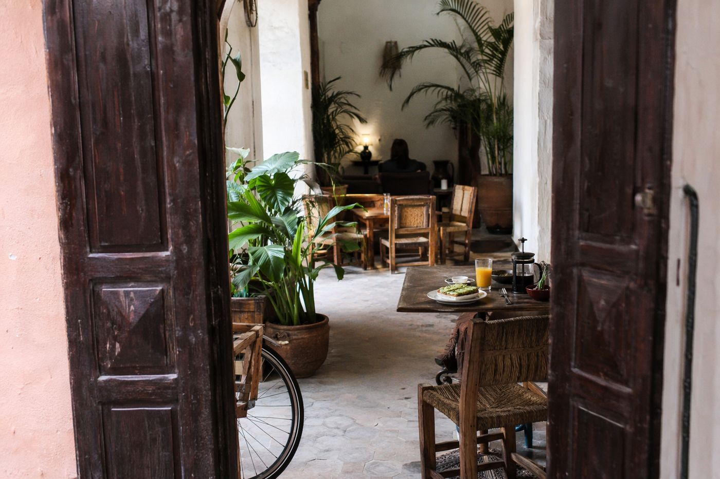 Entrée d'un café de la kasbah vue de la rue, table avec toast à l'avocat et jus d'orange dans la lumière du matin
