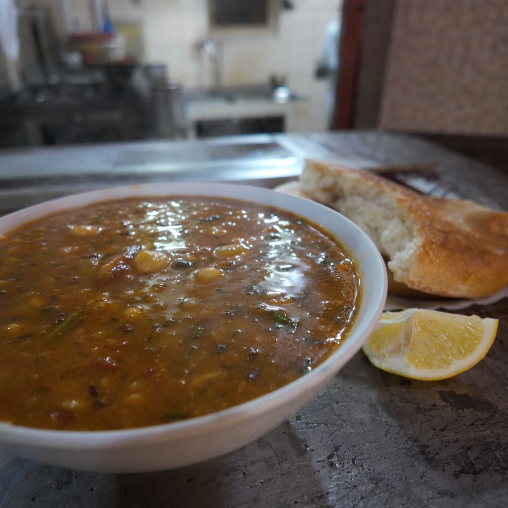 Gros plan sur un bol de harira fumante avec pois chiches et lentilles, citron et pain posés à côté