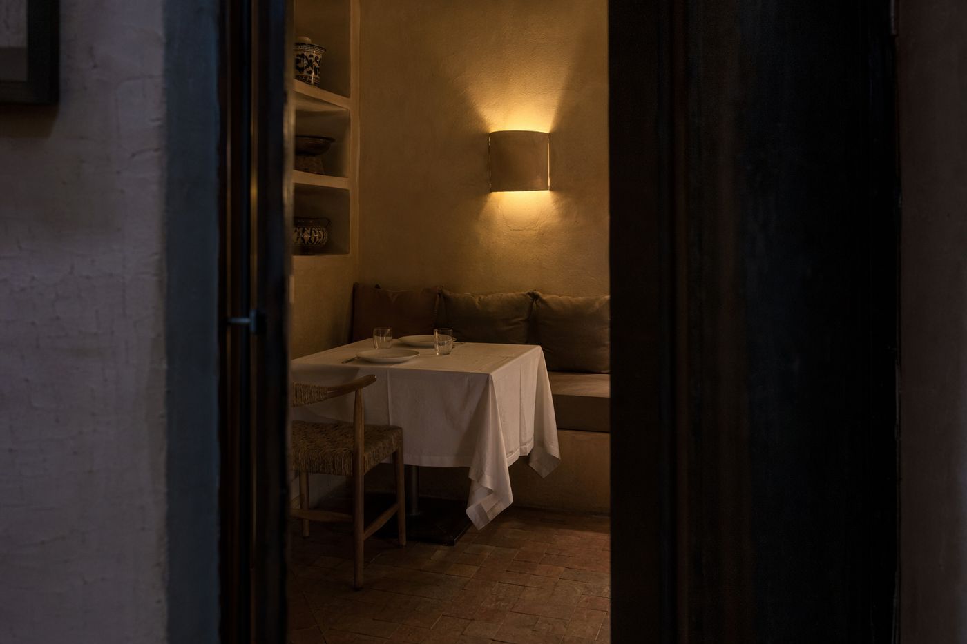 Table pour deux nichée dans un angle calme d'une salle, vue à travers une porte, sous une applique
