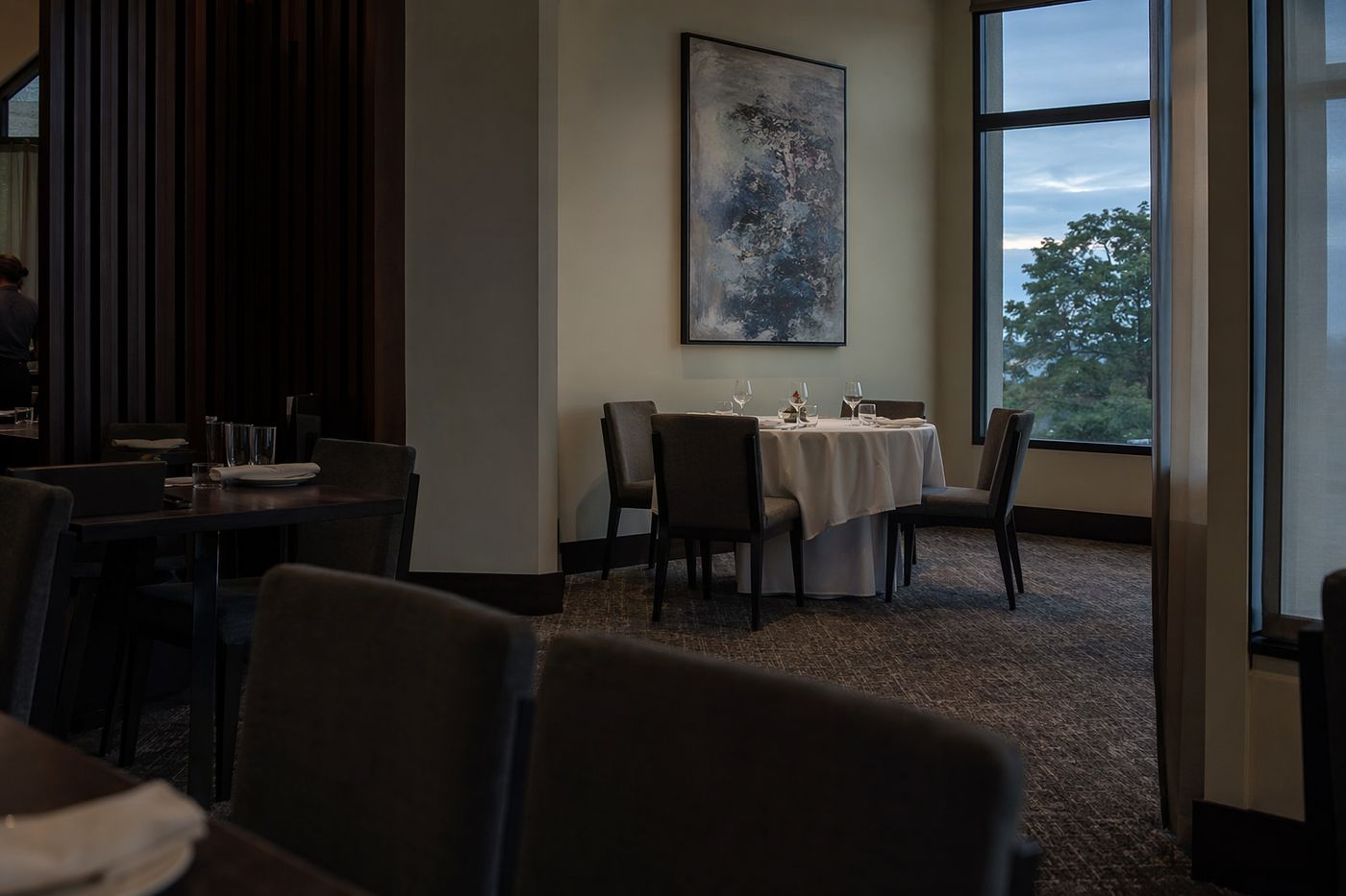Salle de restaurant vide en début de soirée, une table d'angle dressée à l'écart au fond de la pièce