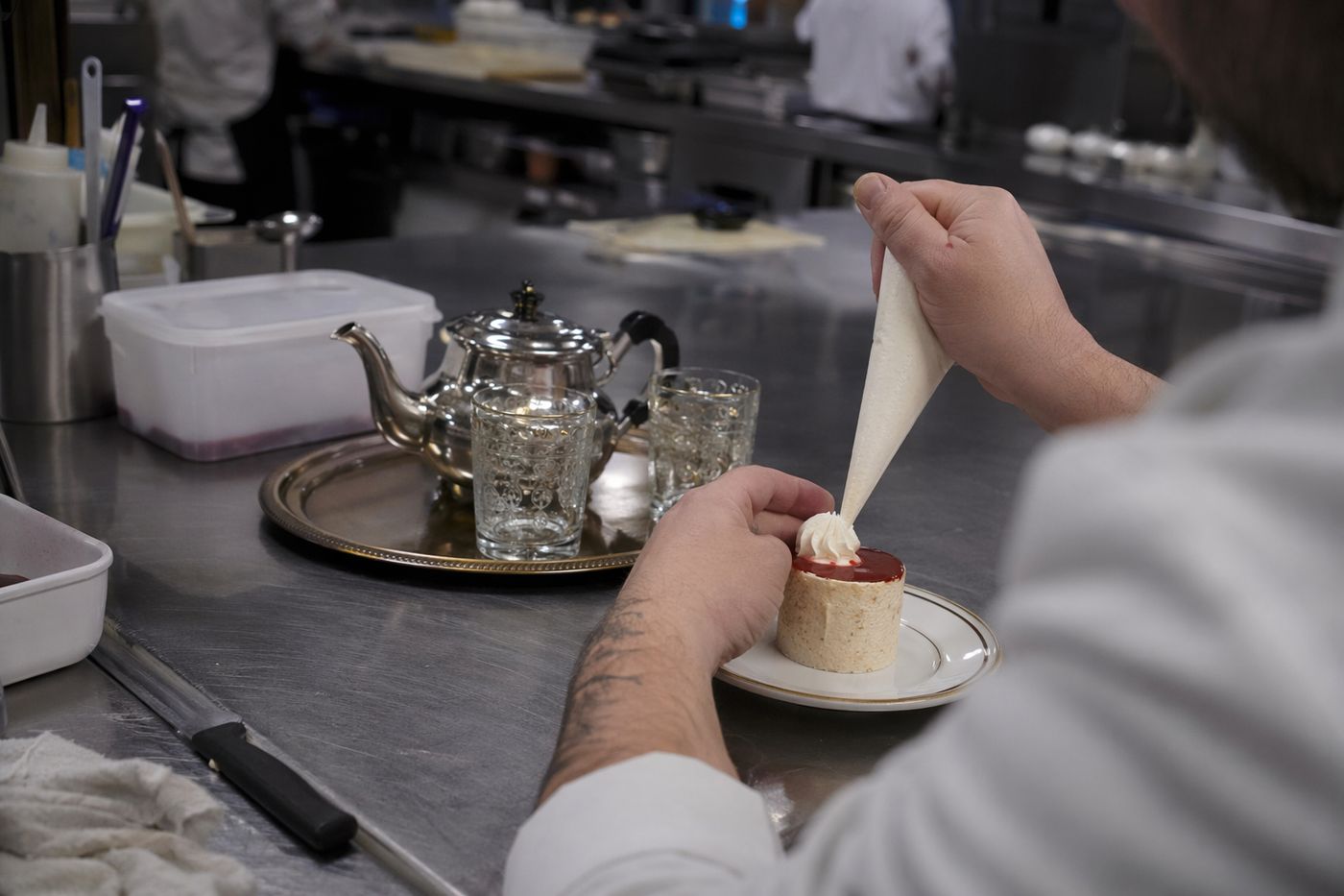 Mains d'un pâtissier terminant un dessert sur le passe d'une cuisine, plateau à thé prêt à côté