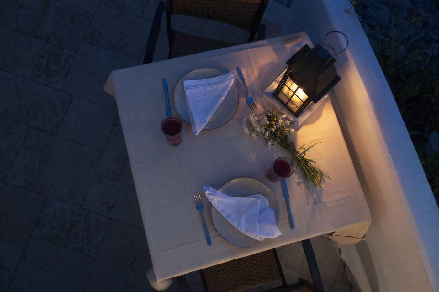 Vue de dessus d'une table pour deux à l'heure bleue, jus de grenade, fleurs blanches et lanterne allumée