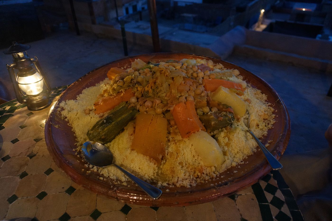 Vue de dessus d'un couscous aux sept légumes sur une table basse de terrasse à la tombée de la nuit