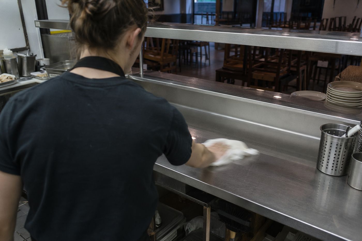 Mains d'un cuisinier essuyant le passe d'une cuisine en fin de service, salle vide et chaises empilées au fond