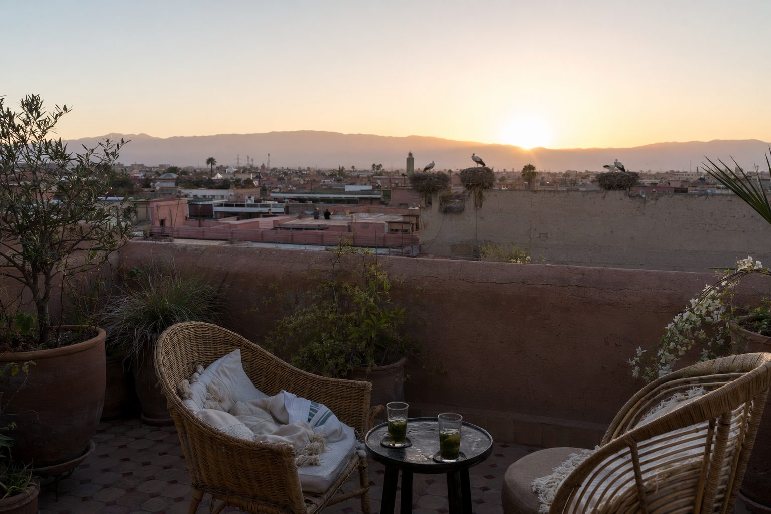 Deux chaises et des verres de thé sur un rooftop face aux toits de Marrakech et à l'Atlas au soleil couchant
