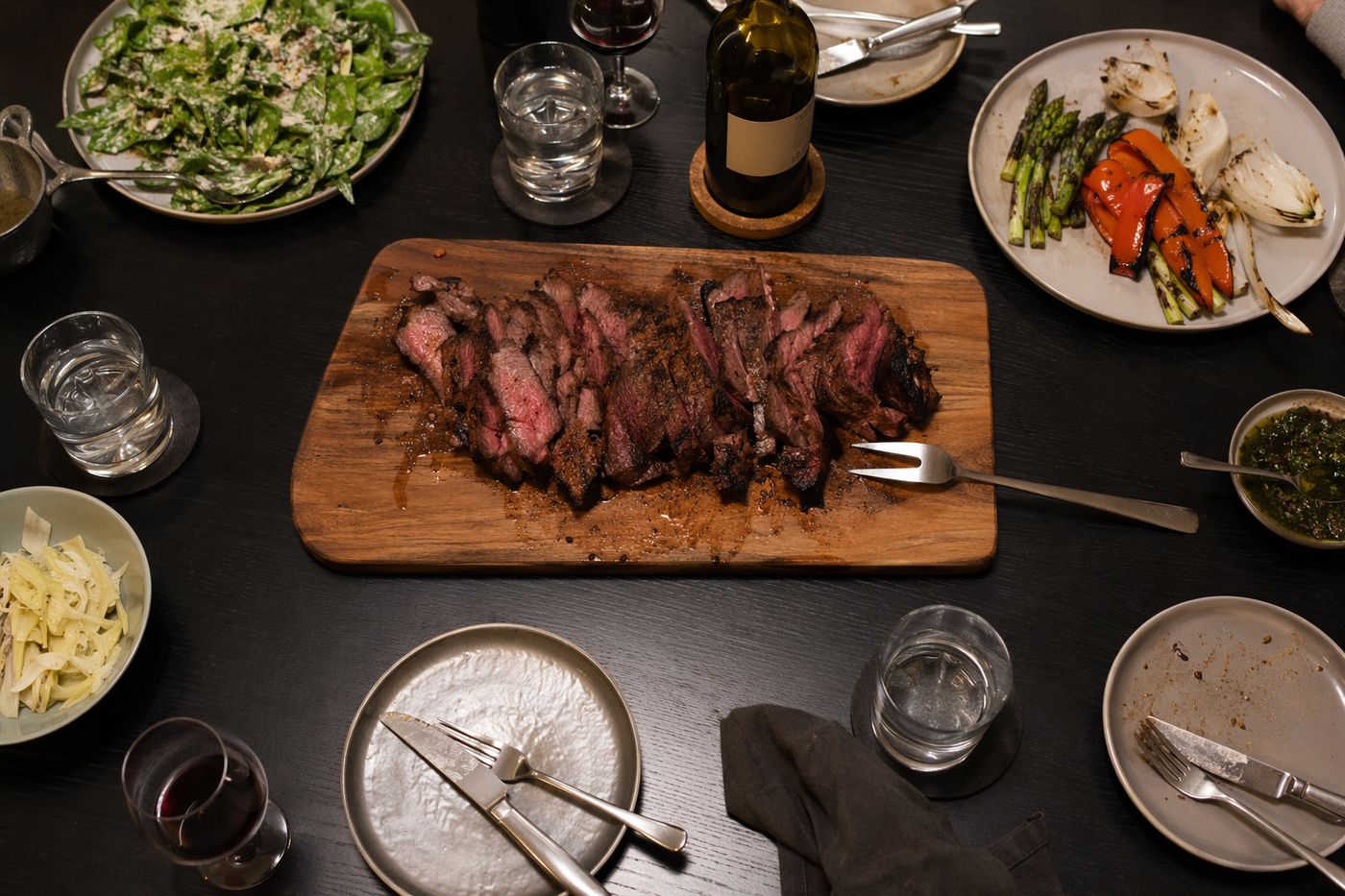 Vue de dessus d'un dîner sobre à partager : bœuf grillé tranché, légumes, salade et verres d'eau