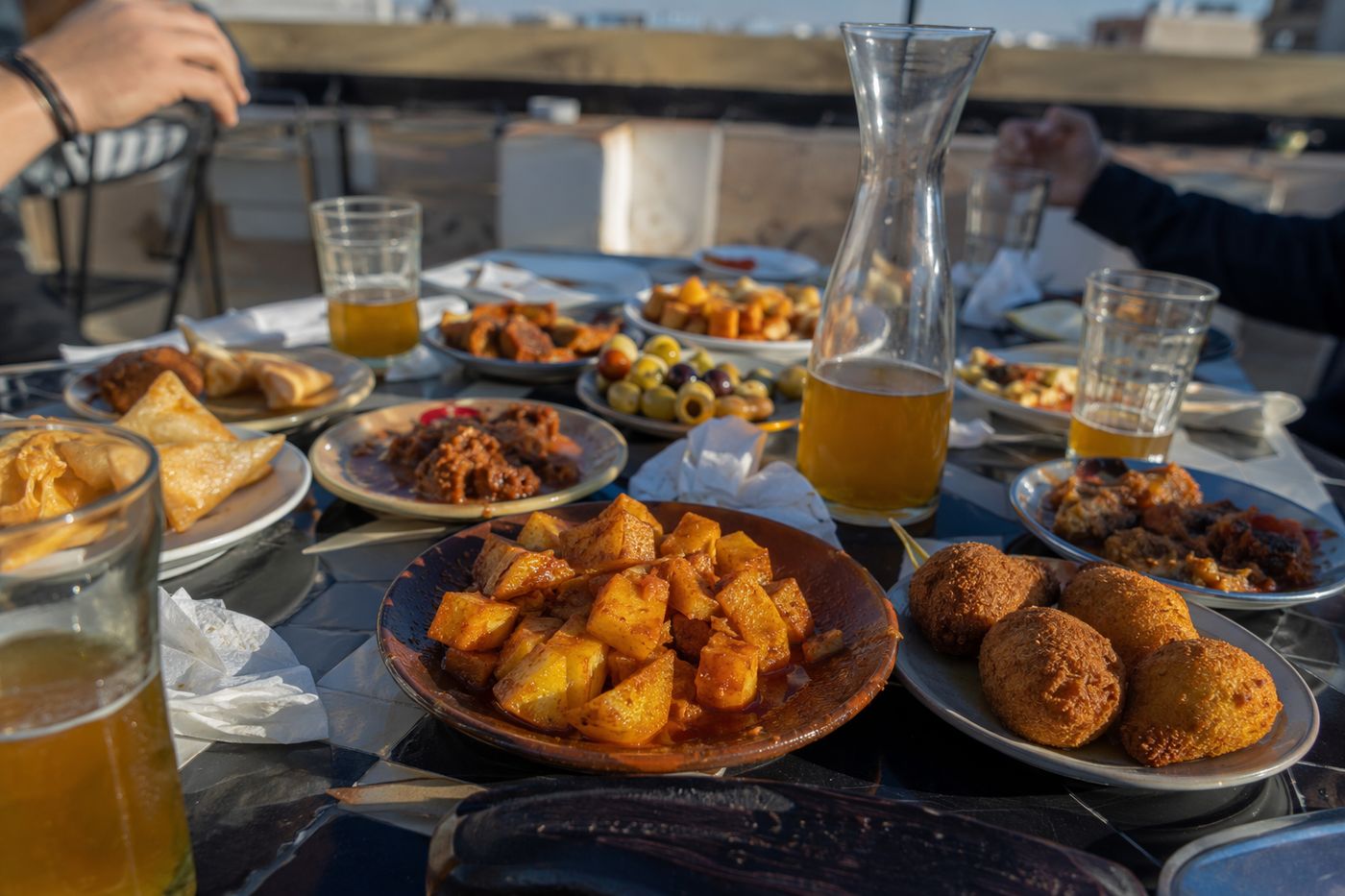 Petite table de rooftop couverte de tapas bon marché en fin d'après-midi, quatre verres et carafe partagée