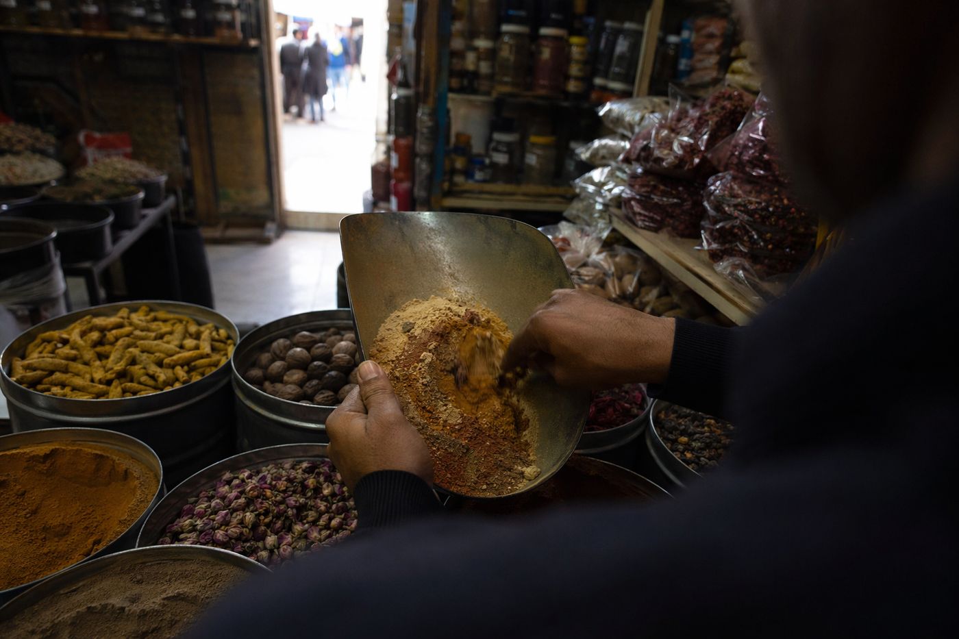 Mains d'un épicier mélangeant du ras el hanout, boutons de rose et muscade dans des boîtes ouvertes.