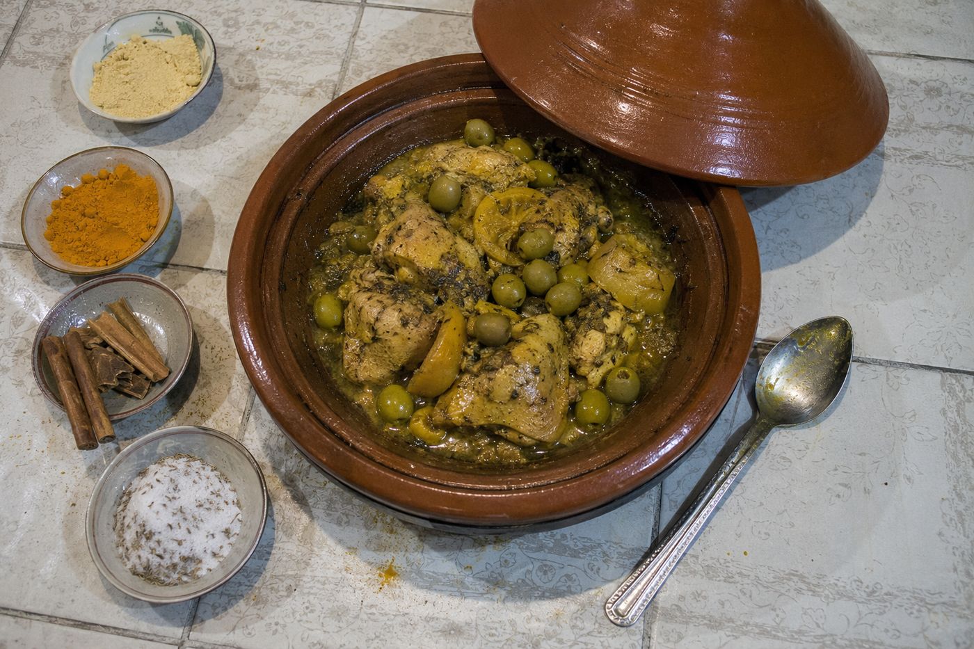 Tajine de poulet au citron confit entouré de bols de gingembre, curcuma, cannelle et sel-cumin, vu du dessus.