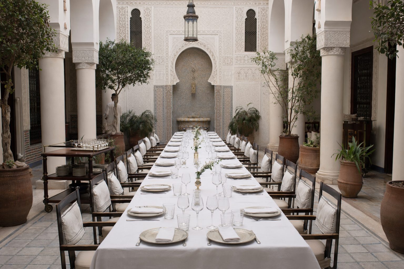 Très longue table unique dressée pour un groupe dans le patio à colonnes d'un riad-restaurant, avant le service