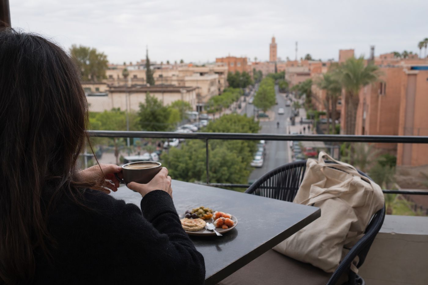 Café et petite assiette sur une terrasse tranquille en hauteur, avenue arborée floue en contrebas.