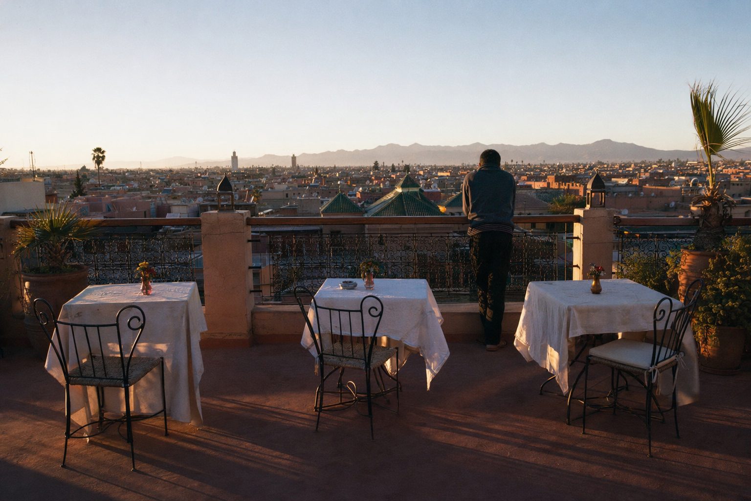 Terrasse de toit presque vide au soleil couchant, silhouette au parapet face aux toits et à l'Atlas.