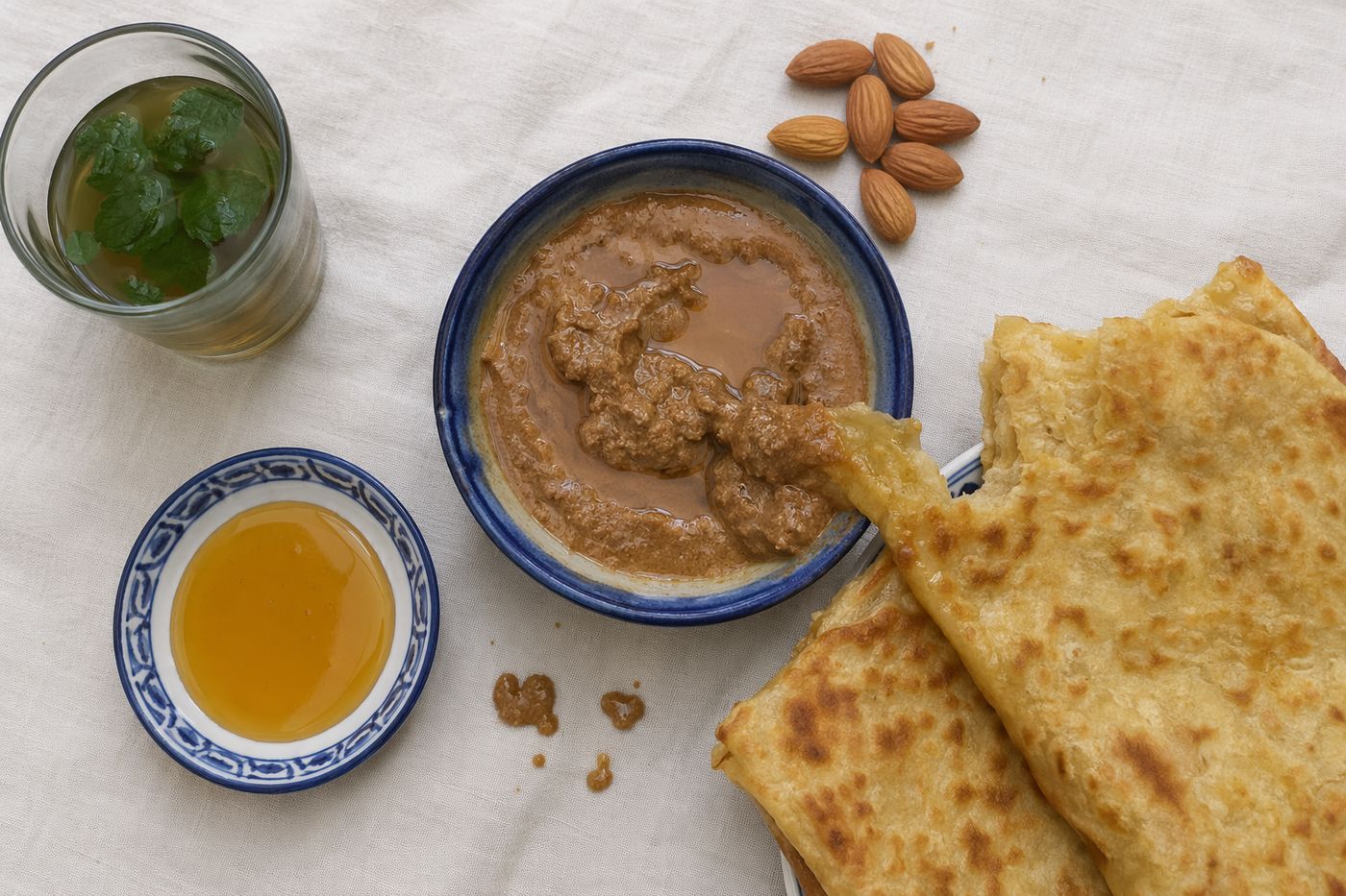 Bol d'amlou, msemen déchiré et trempé, miel, amandes et thé à la menthe vus du dessus.