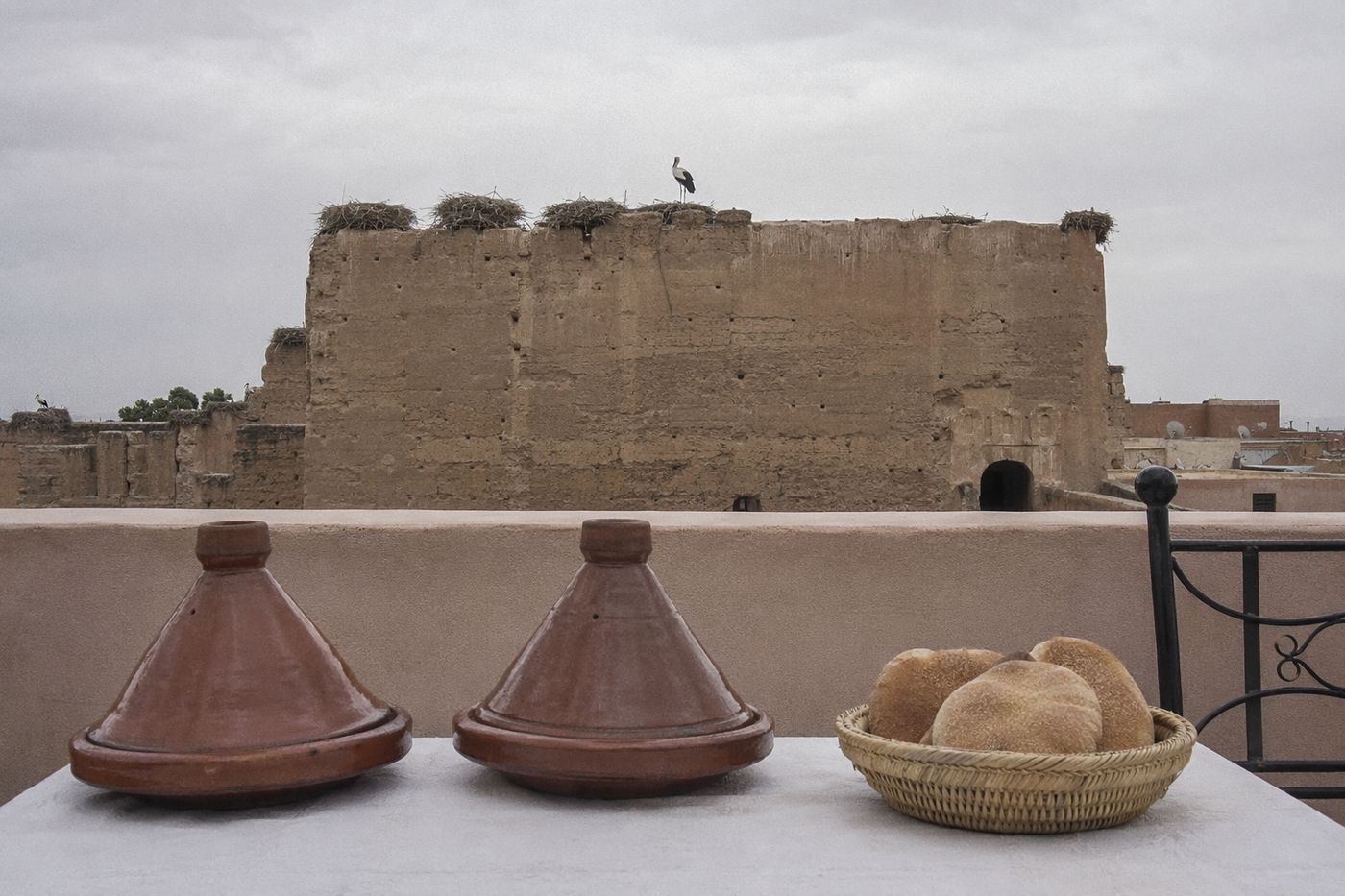 Tajines sur une table de rooftop face aux remparts et aux nids de cigognes, ciel couvert