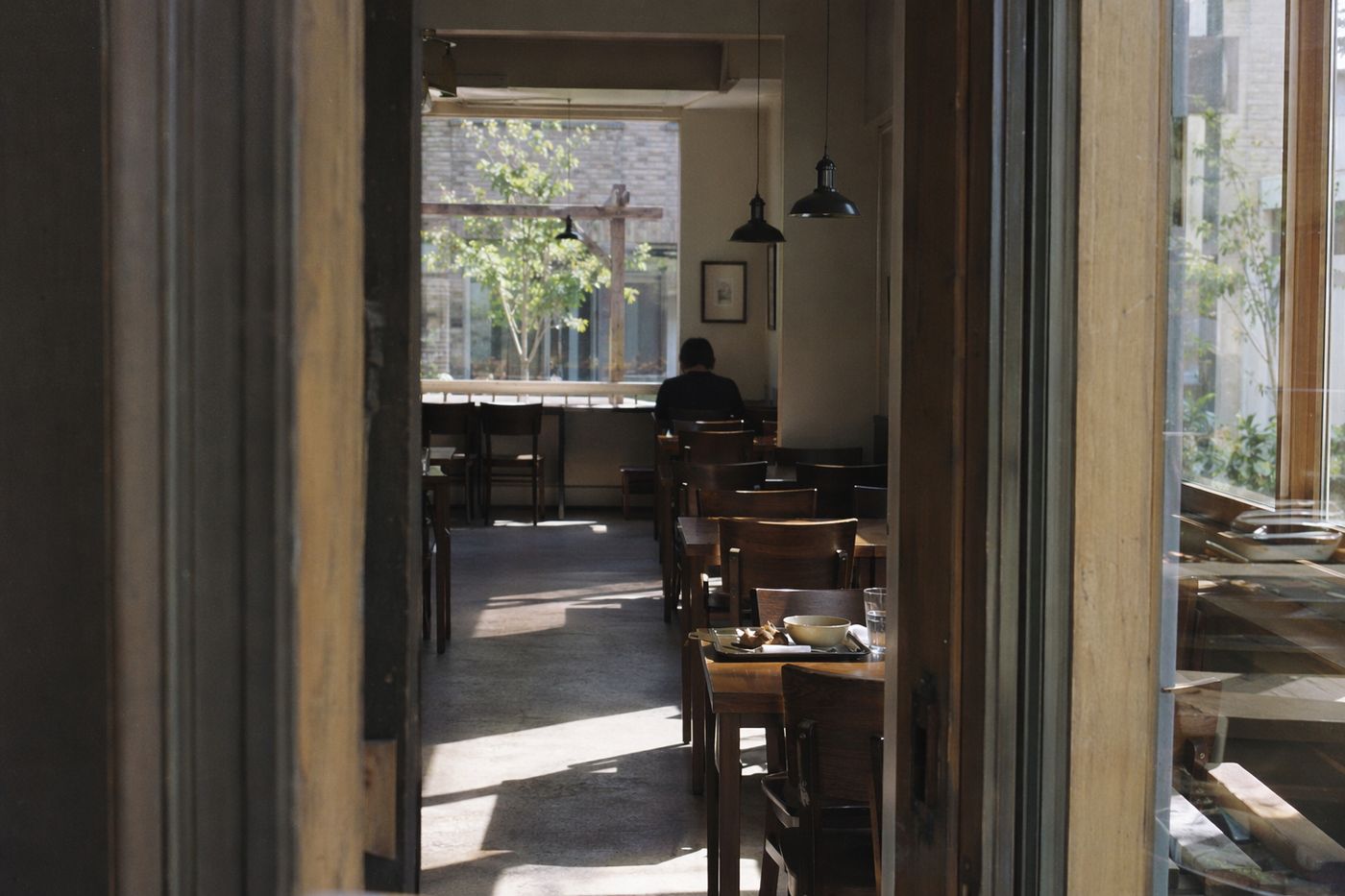 Salle de café presque vide à 15 heures vue depuis la porte, soleil rayant le sol entre les tables