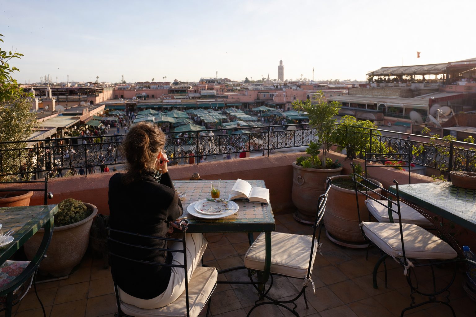 Personne seule attablée de dos au bord d'un rooftop, livre ouvert et thé à la menthe au-dessus d'une place