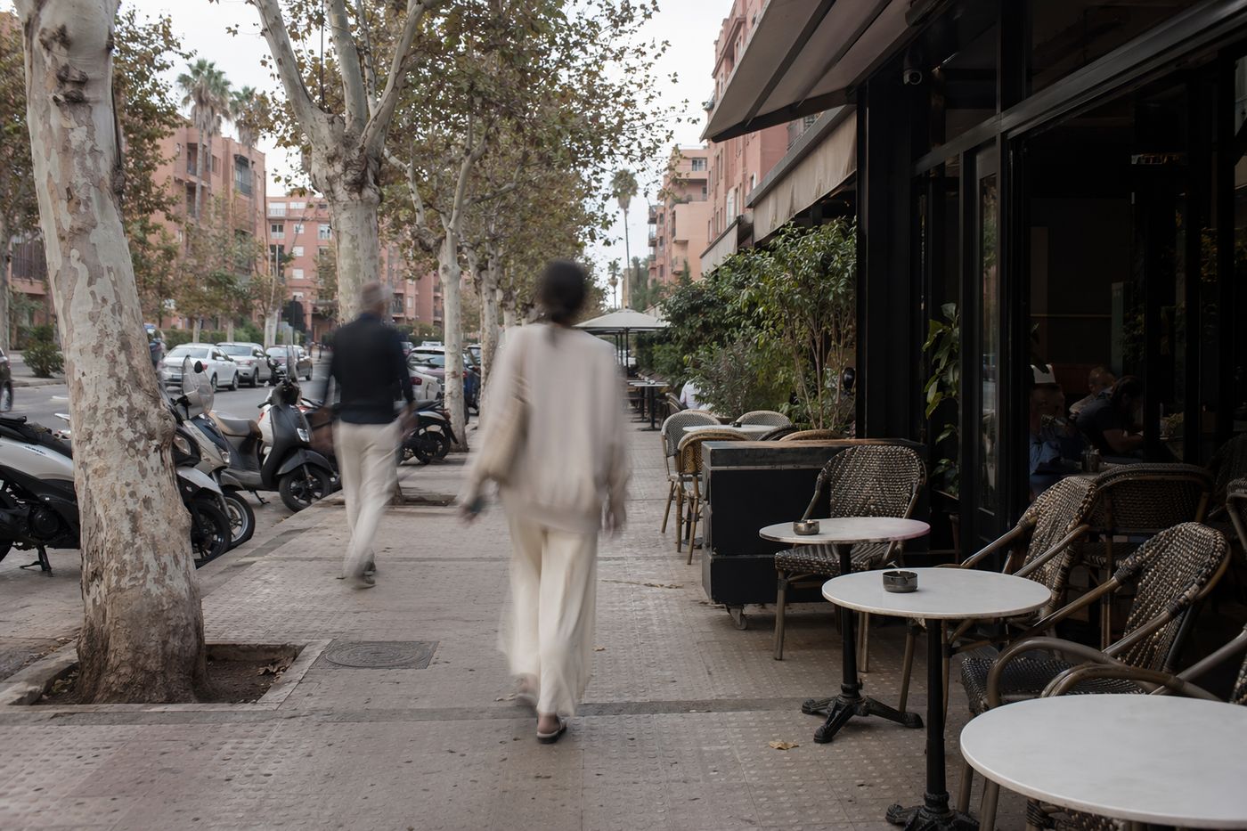 Terrasse de café sur un large trottoir arboré de la ville nouvelle, passants en léger flou.