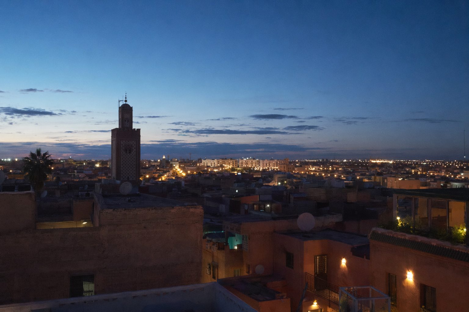 Toits de la médina et minaret à l'heure bleue, les lumières de la ville nouvelle au loin.