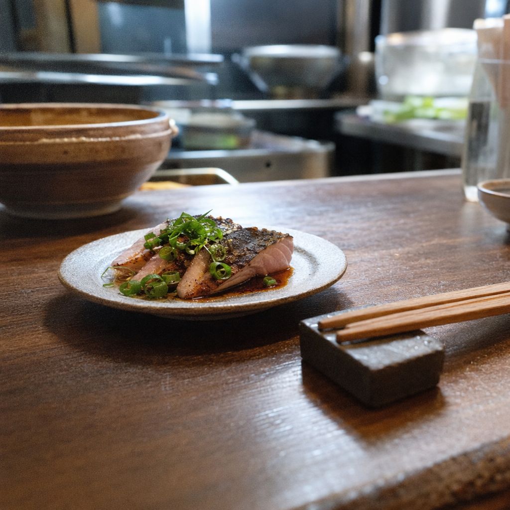 Gros plan d'une assiette de poisson saisi et baguettes au bord d'un comptoir de cuisine ouverte.