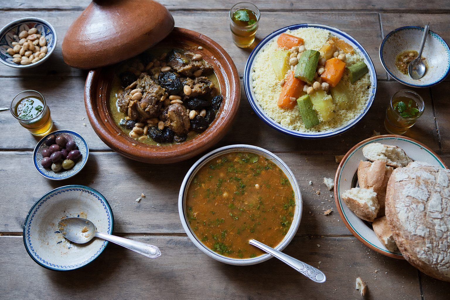 Vue du dessus d'une table marocaine : tajine, couscous, harira, pain et thé à la menthe.