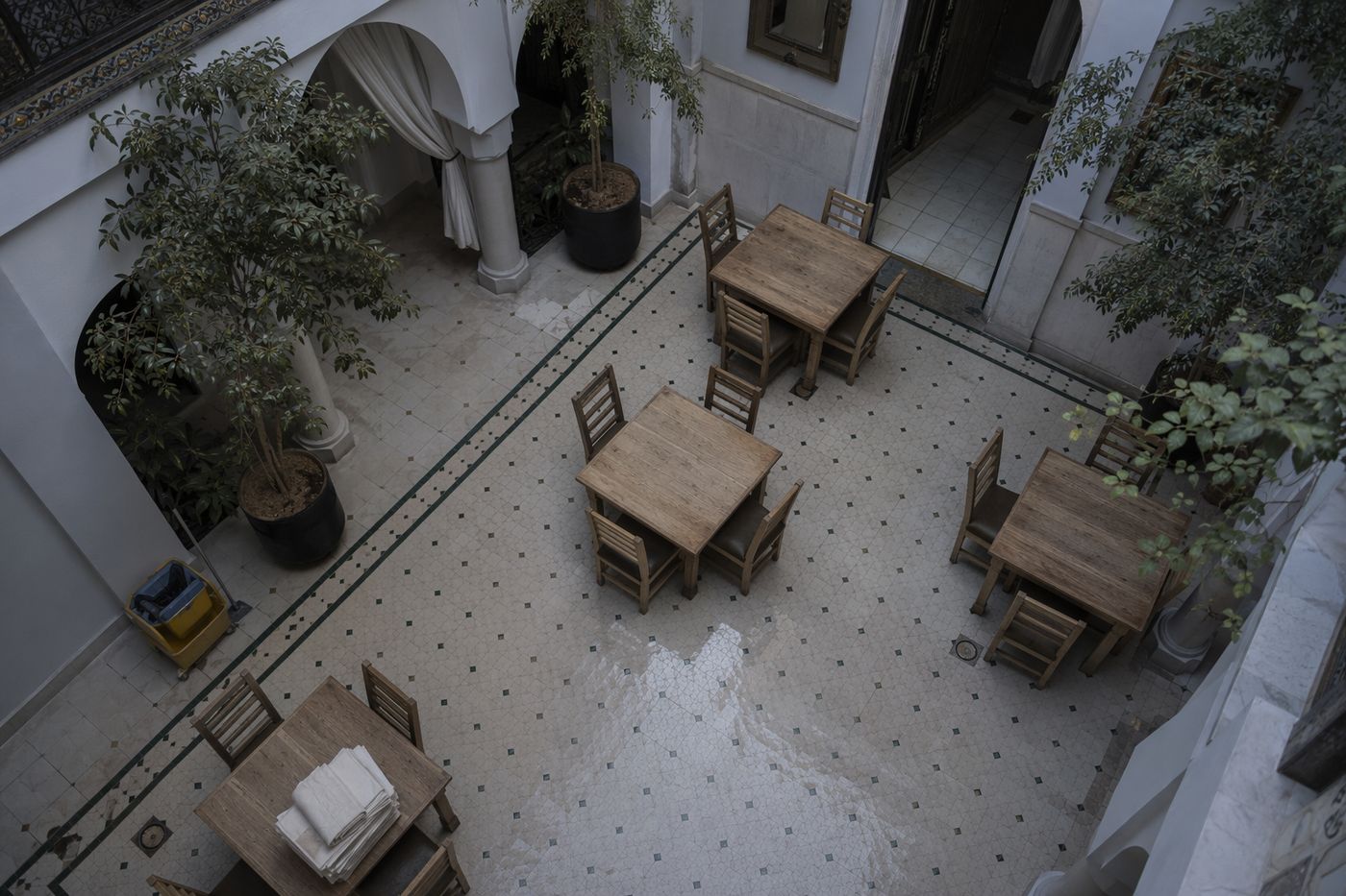 Patio de restaurant vide au matin, nappes pliées et sol carrelé encore humide avant le service