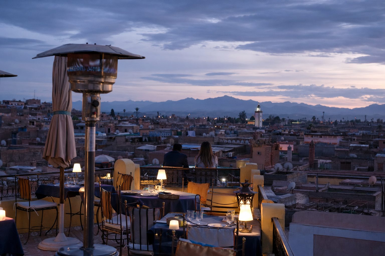 Terrasse de toit dressée pour le dîner à l'heure bleue, toits de la médina et Atlas au loin
