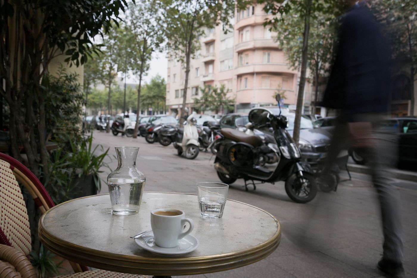 Table de bistrot sur un trottoir d'avenue de Guéliz sous un ciel couvert, scooters flous en arrière-plan