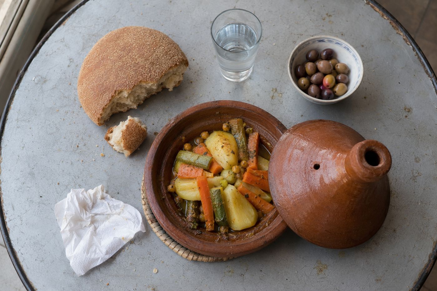 Tajine de légumes, pain et olives sur une table métallique simple, lumière du matin