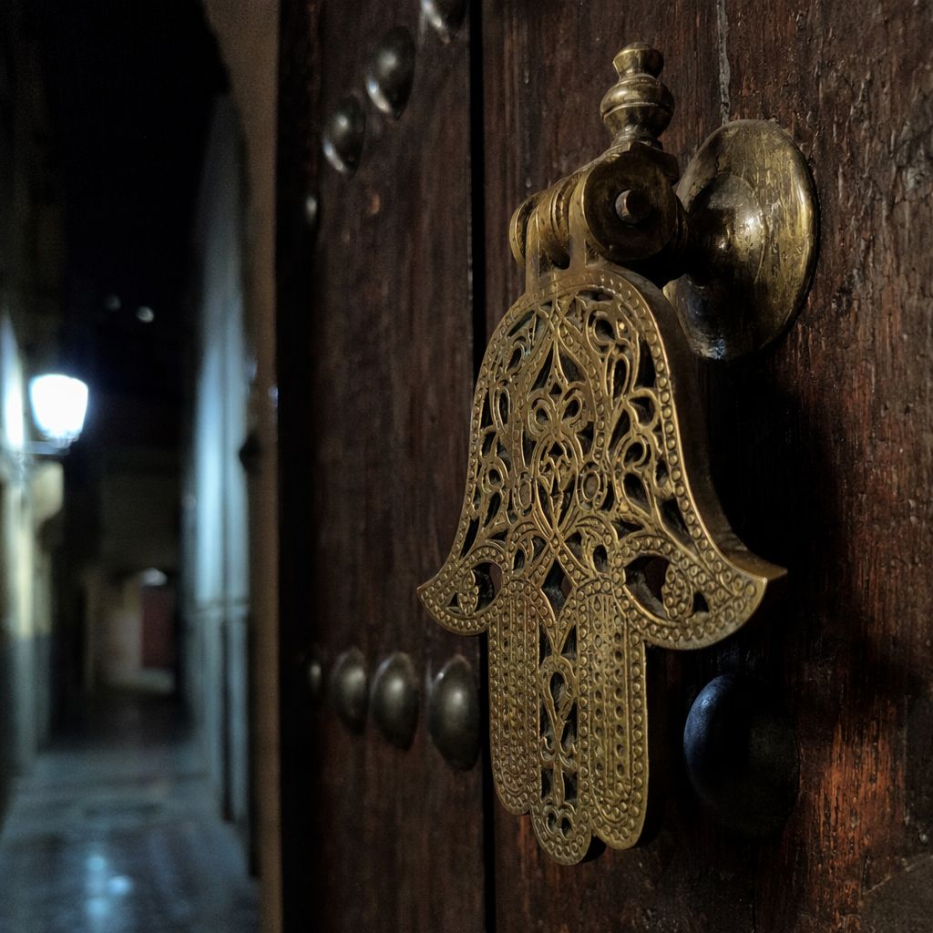 Heurtoir en laiton sur une porte de riad cloutée, éclairé de nuit par une lampe murale