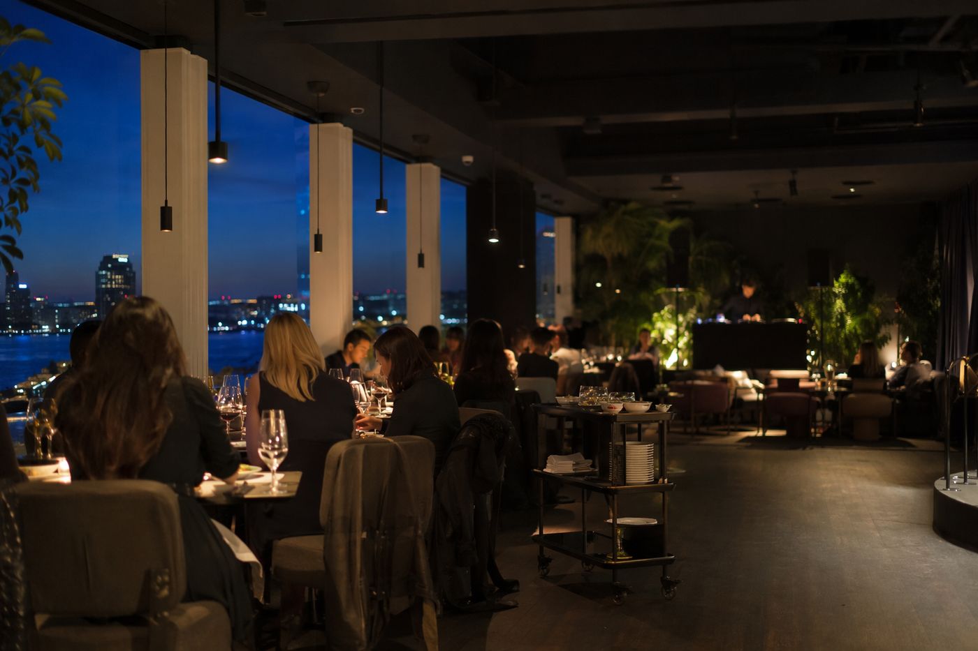 Intérieur de dîner-club contemporain à l'heure bleue, tables devant et cabine de DJ floue au fond.