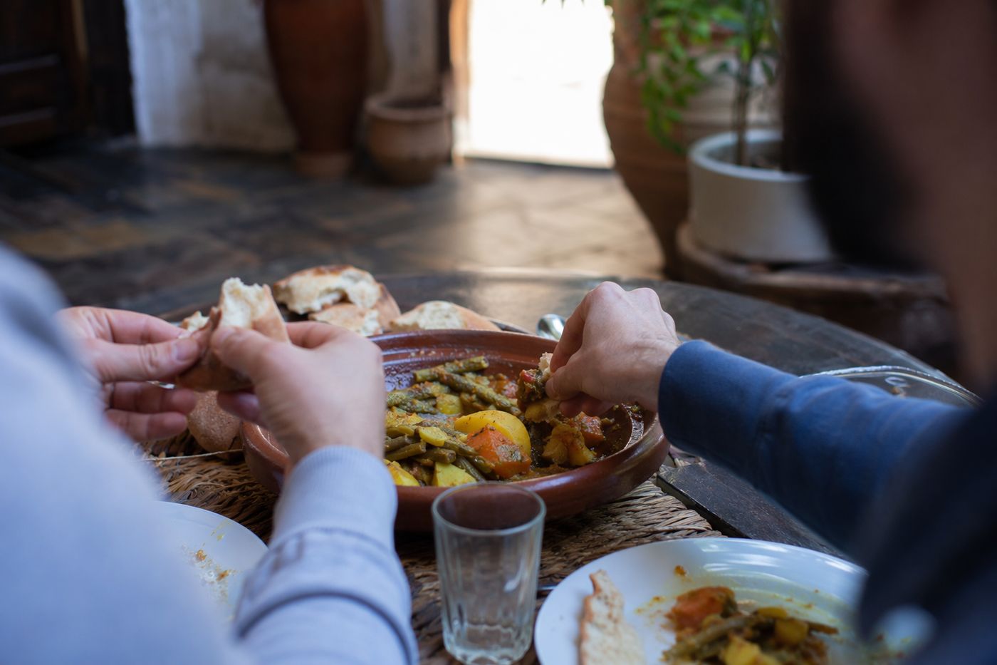 Mains rompant du khobz pour saisir une bouchée dans un tajine commun posé au centre de la table.