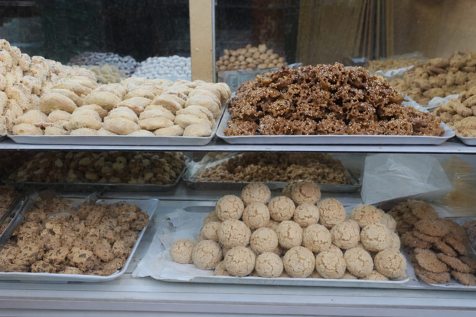 Vitrine de pâtisserie de la médina : cornes de gazelle, chebakia au sésame et ghribas craquelées sur plateaux.