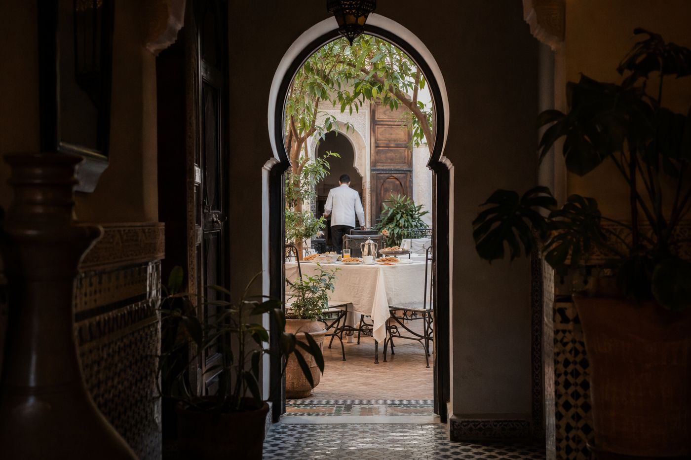Porte en arc d'un riad ouvrant sur un patio clair où une table de petit-déjeuner est dressée.