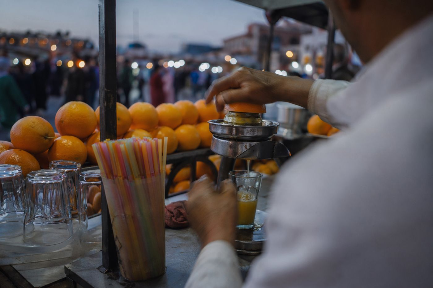 Mains d'un vendeur pressant des oranges sur une charrette à l'aube, verre de jus en cours de remplissage.