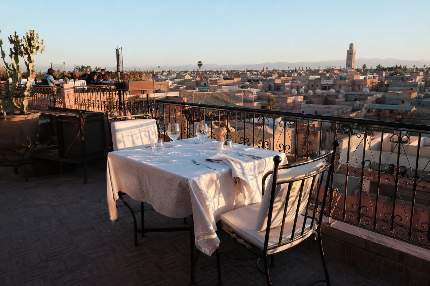 Table dressée pour deux au bord d'une terrasse de rooftop, toits de la médina et minaret avant le coucher du soleil