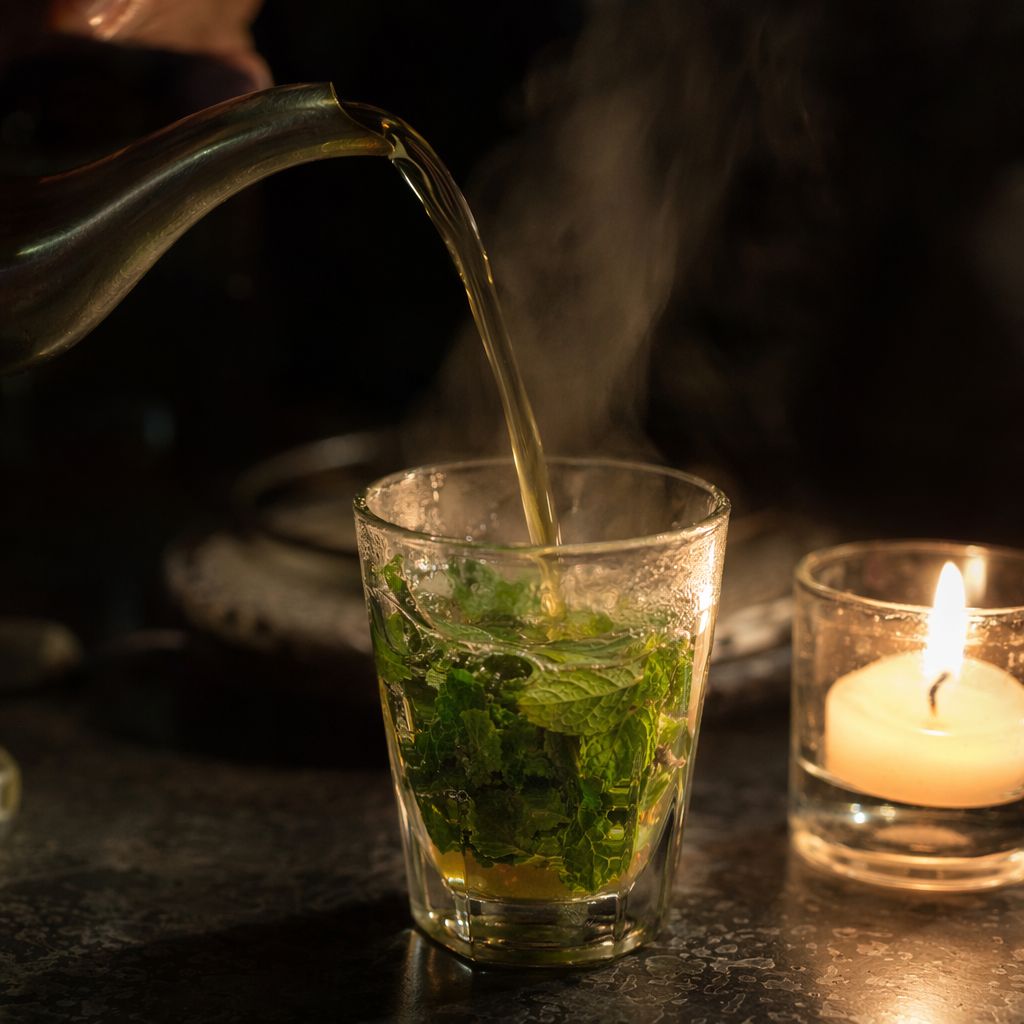 Thé à la menthe versé de haut dans un verre à la bougie, filet de thé en mouvement et vapeur