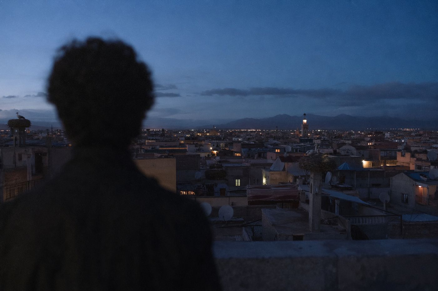 Silhouette de dos au bord d'un rooftop regardant la médina à l'heure bleue, premières lumières de la ville
