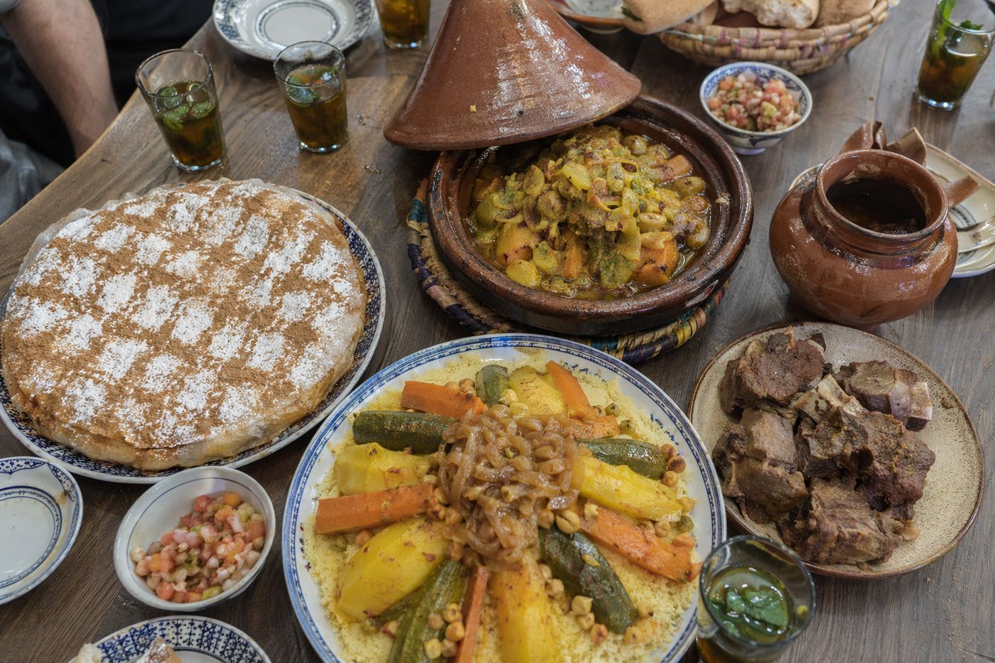 Vue de dessus des plats emblèmes : pastilla, tajine, couscous aux sept légumes et tanjia avec pain et thé