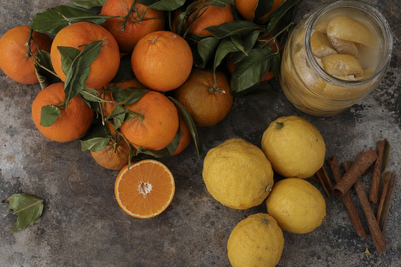 Oranges avec feuilles, citrons et bocal de citrons confits en saumure vus du dessus, bâtons de cannelle.