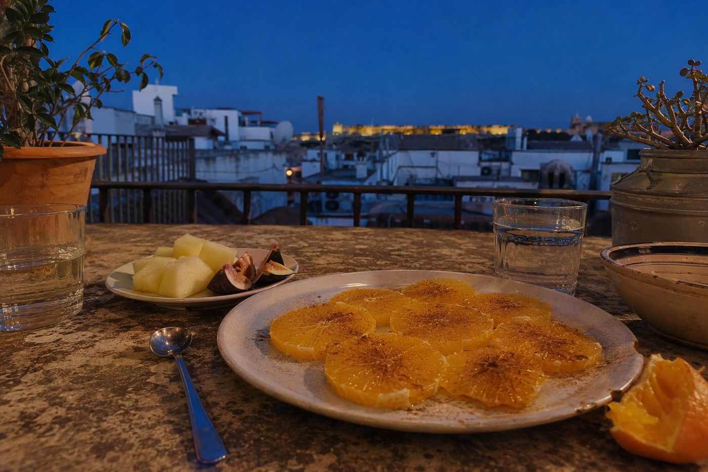 Salade d'oranges à la cannelle et assiette de figues et melon sur une table de terrasse au crépuscule.