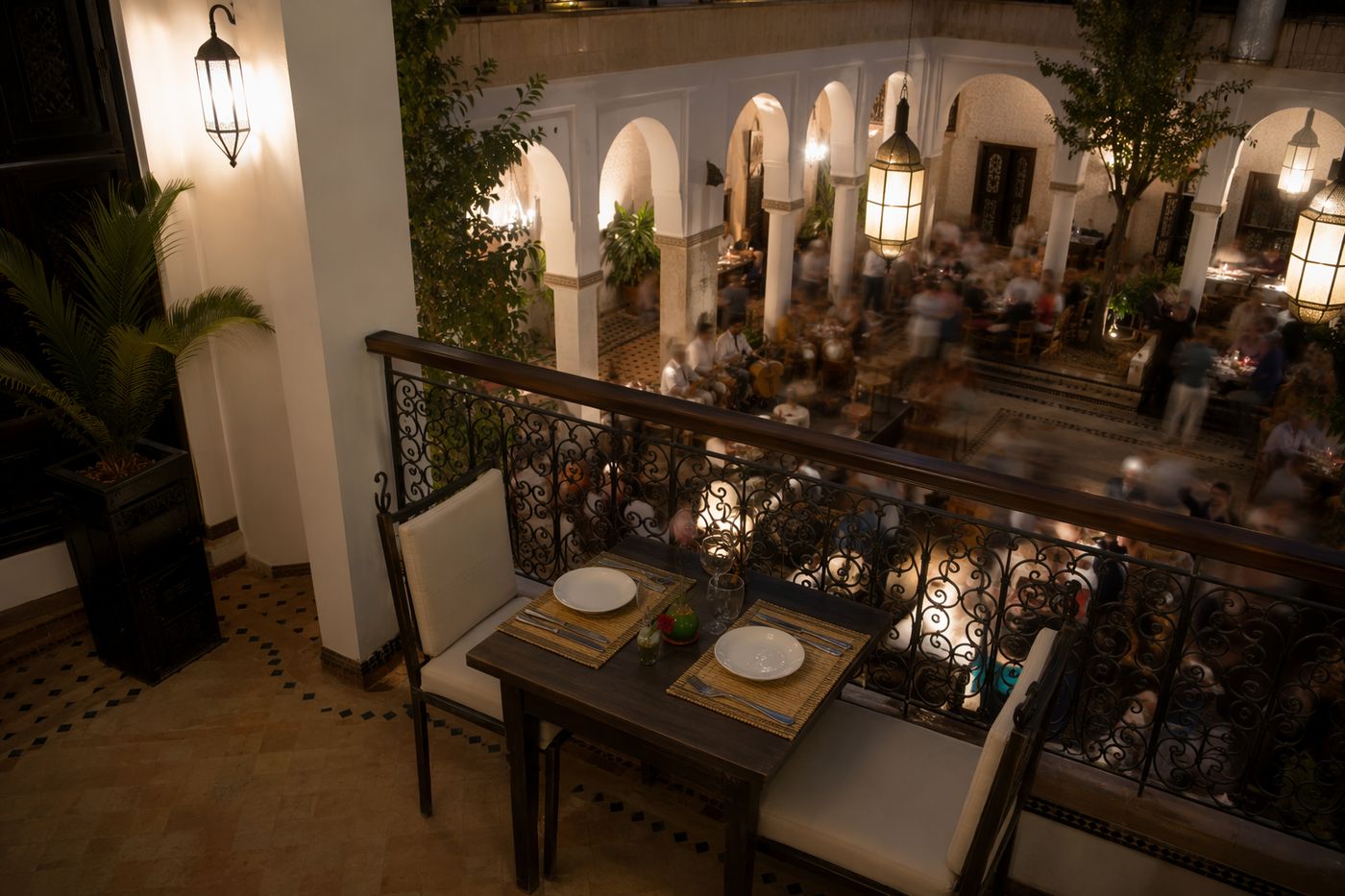 Depuis un salon à l'étage, table calme au premier plan et patio animé flou de mouvement en contrebas