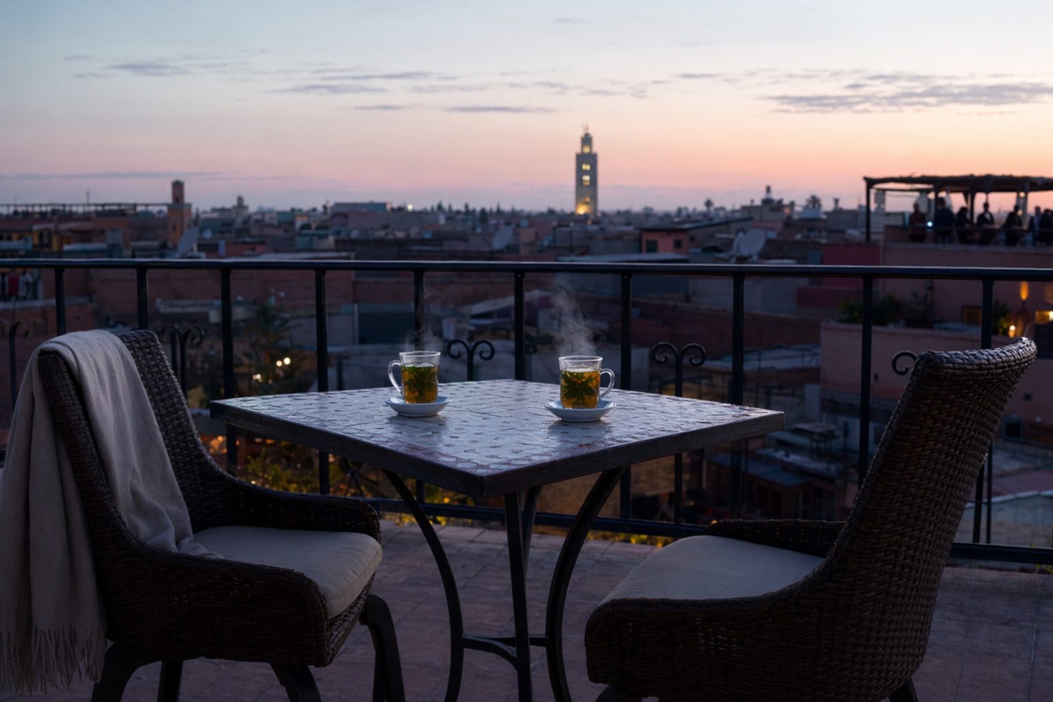 Table pour deux au bord d'un rooftop après le coucher du soleil, deux verres de thé fumants et ciel rose pâle sur la médina